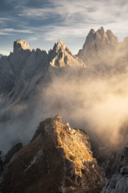 Escursionista solitario su un'aguzza cresta rocciosa delle Dolomiti circondata da nebbia al tramonto dorato, fotografia di paesaggio di Carlo Pagliuca