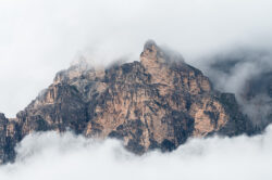 Imponente e dettagliata parete rocciosa verticale dolomitica che emerge dalla fitta nebbia, scatto tecnico di fotografia di territorio