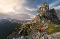 Escursionista in giacca rossa osserva il panorama dolomitico verso il Passo Giau e l'Averau al tramonto, fotografia lifestyle outdoor