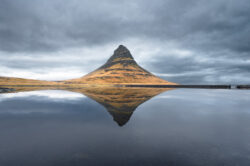La montagna Kirkjufell perfettamente riflessa nell'acqua calma sotto un cielo nuvoloso, icona della fotografia di paesaggio islandese