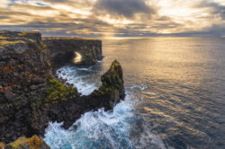 Imponente scogliera lavica islandese con arco naturale e faraglione a picco sul mare dorato, fotografia di territorio