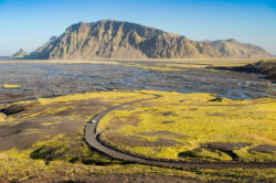 Strada sterrata a serpentina che attraversa una vasta piana alluvionale islandese verso le montagne, fotografia di territorio e viaggio